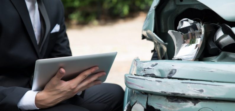 insurance claim - adjuster with tablet examining damaged car