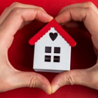 small home model in middle of hands shaped as a heart