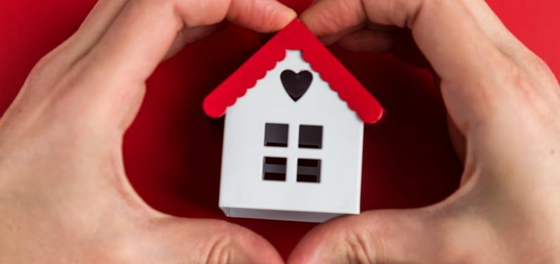 small home model in middle of hands shaped as a heart