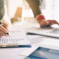 businesswoman reviewing clipboard of papers and using laptop