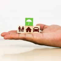 insurance concept hand holding blocks with umbrella, house, car, and family icons