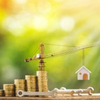 model crane holding up a model house next to a stack of coins