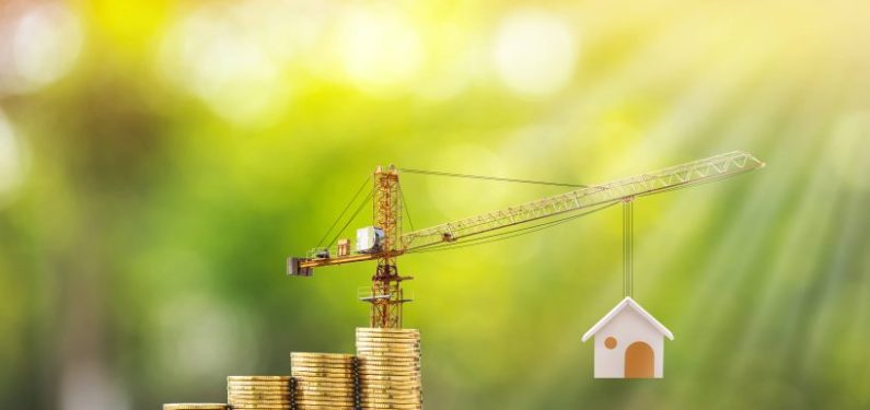 model crane holding up a model house next to a stack of coins