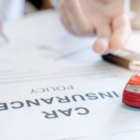 person signing car insurance policy documents and a small toy car