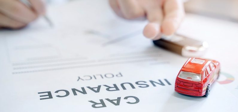 person signing car insurance policy documents and a small toy car