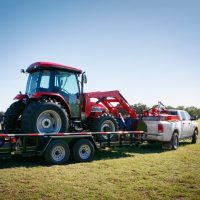 pickup truck hauling a red tractor on a flatbed trailer