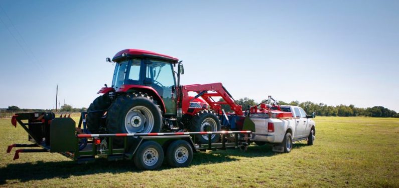 pickup truck hauling a red tractor on a flatbed trailer